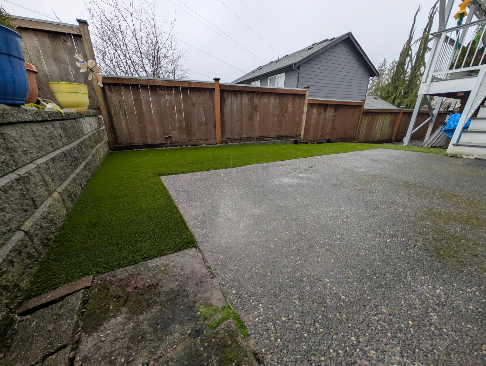 Residential backyard in Everett WA with K9Grass Classic+ pet turf installed along wood fence beside concrete patio and retaining wall.
